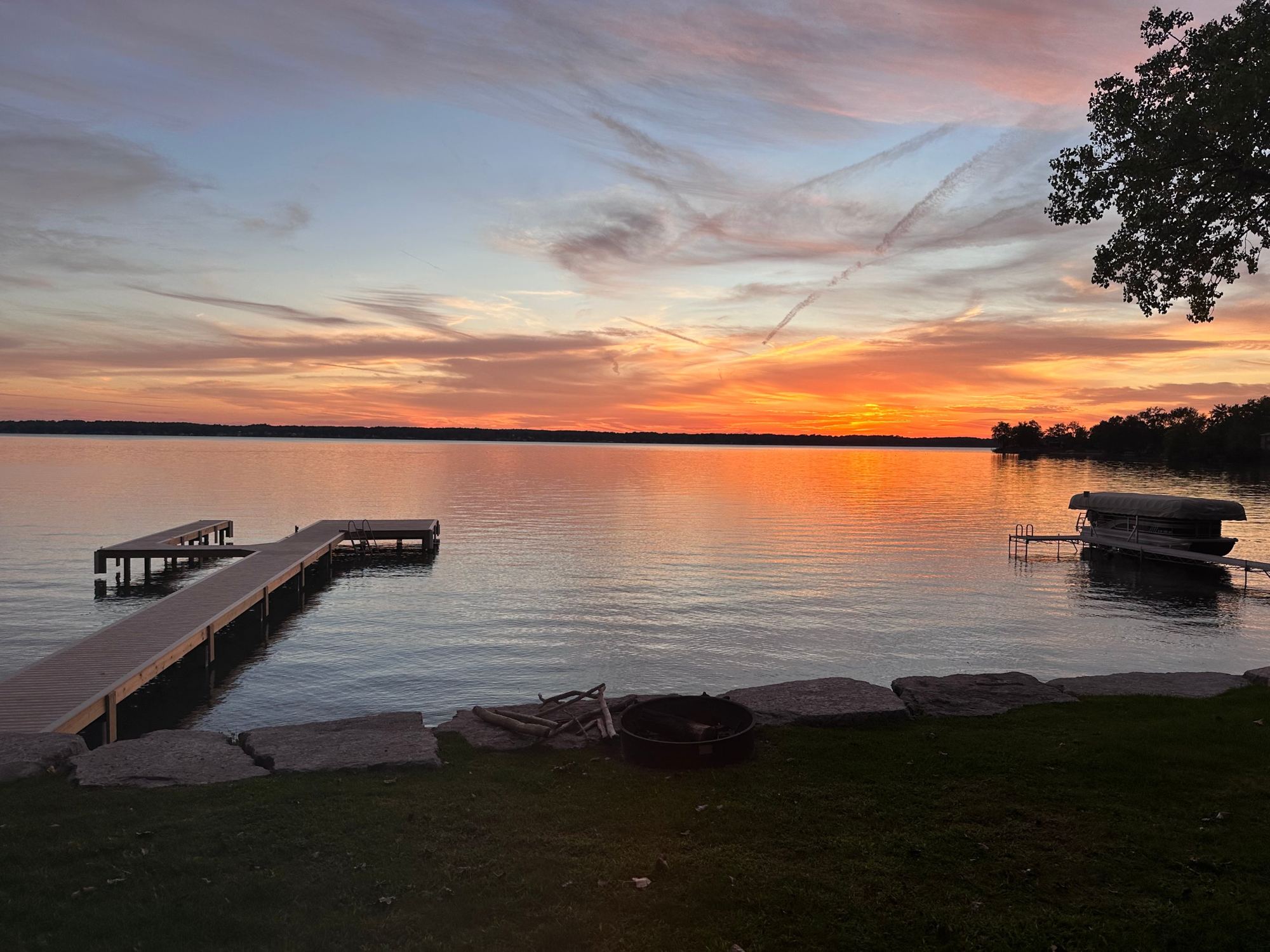 Sunset over Cayuga Lake from the lawn, with the private dock, a fire pit at the water's edge and a covered pontoon boat